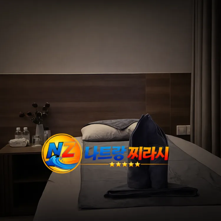 Hotel room with a made bed, decorative towel fold and pillow on a gray bed runner; bedside table with water bottles and flowers; a colorful logo overlays the scene