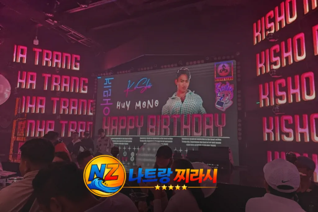 Nightclub birthday party scene with a large screen displaying a person and 'Happy Birthday' text, surrounded by pink neon signs.